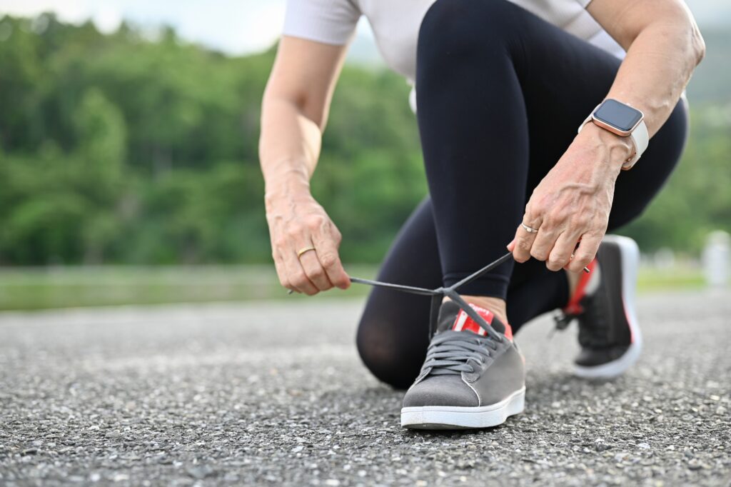 Healthy aged woman tying her running shoes on the road in the greenery park.